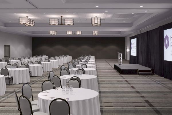 A large conference room with round tables, chairs, a stage, and 