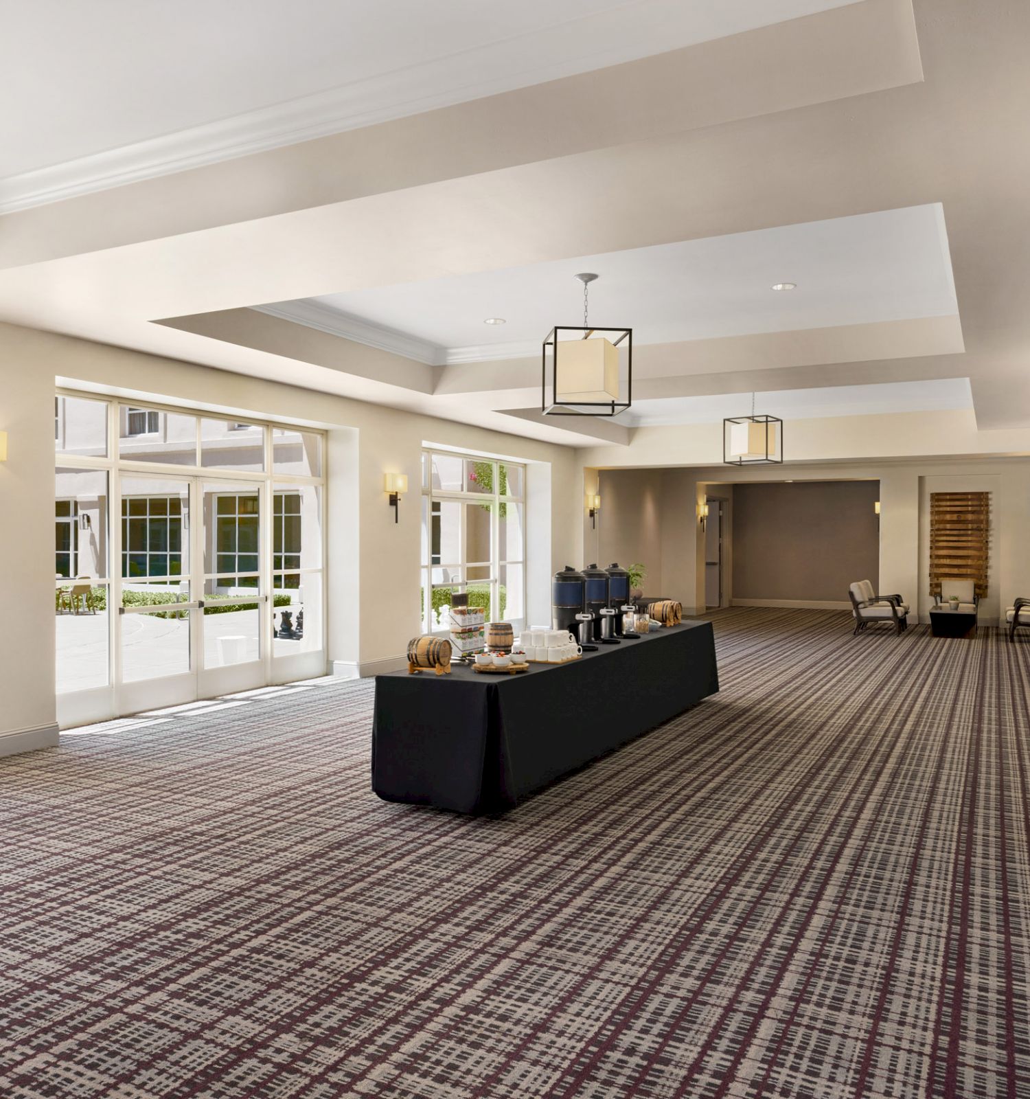 This image shows a spacious, elegant room with large windows, carpeted floors, and a table in the center. The room is well-lit with soft lighting.