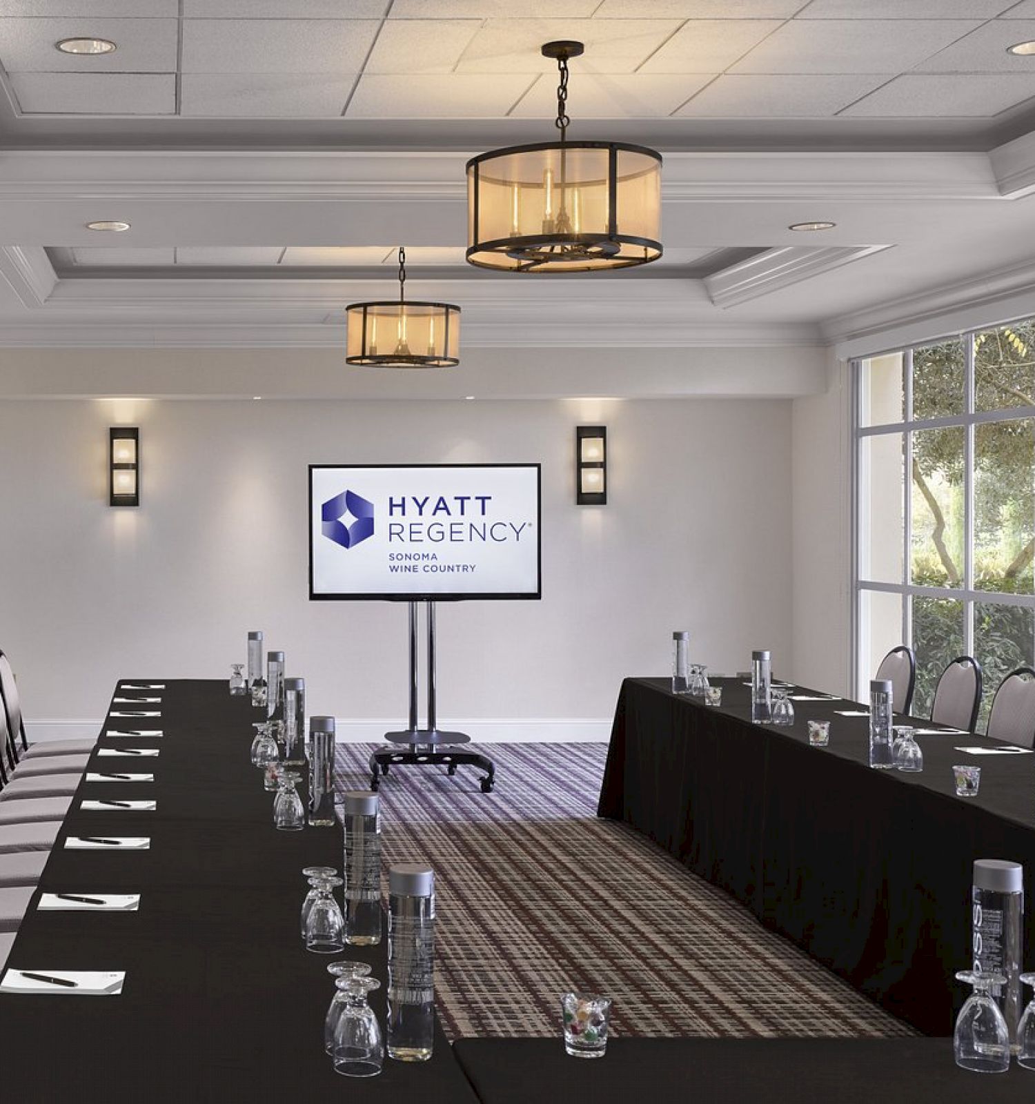 A conference room with a long U-shaped table setup, chairs, water pitchers, glasses, and a screen displaying 