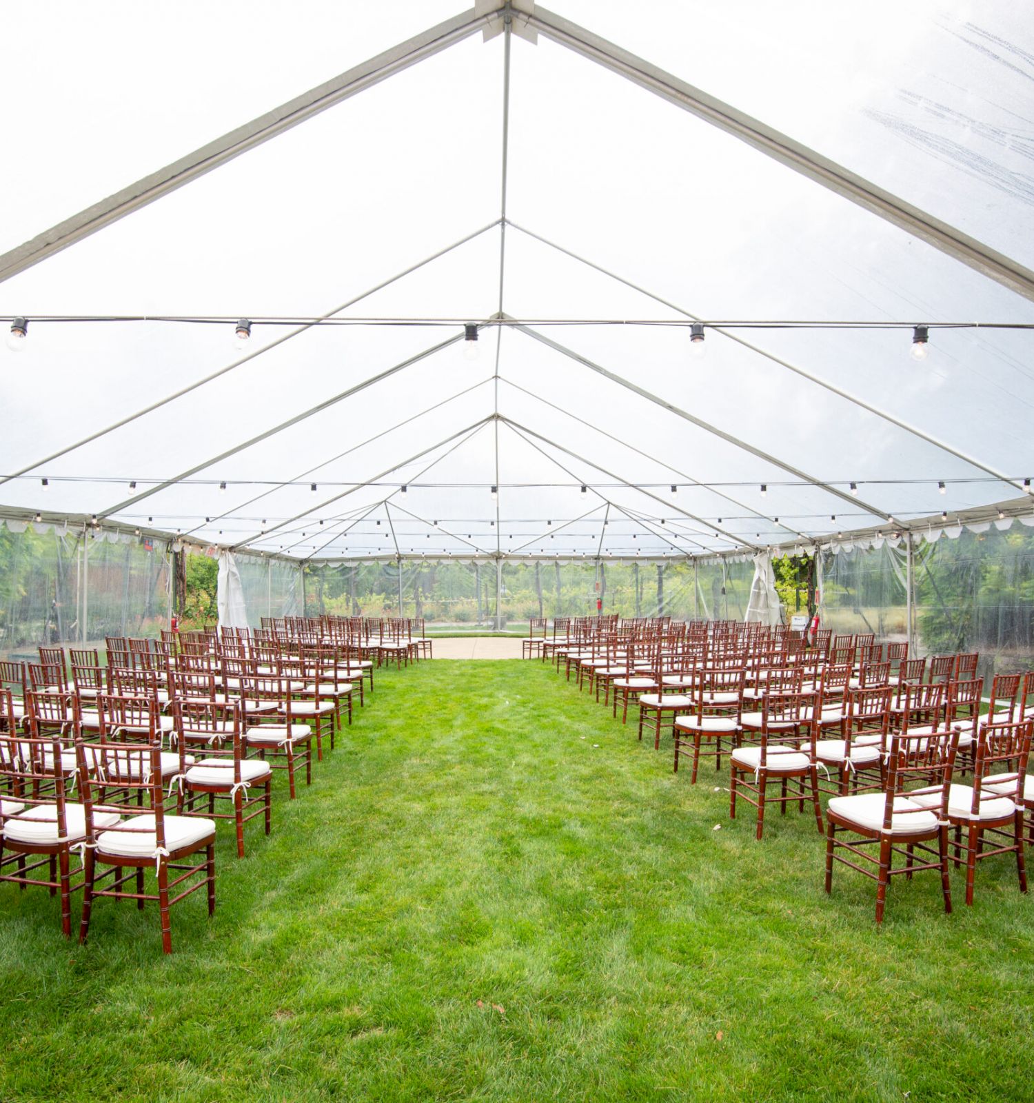 The image shows an outdoor setup with rows of chairs under a large transparent tent, likely arranged for an event such as a wedding or ceremony.