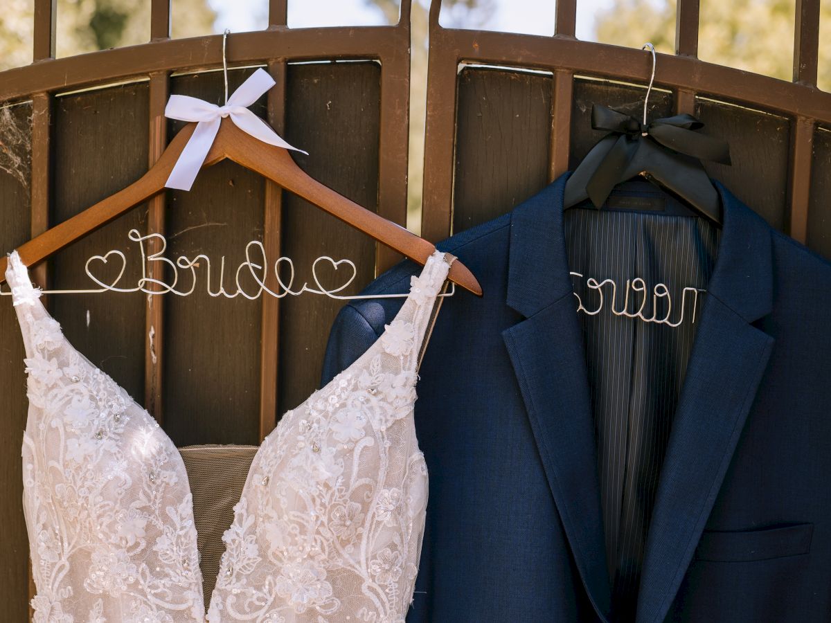 Wedding attire hanging on personalized wire hangers: a white lace wedding dress labeled 