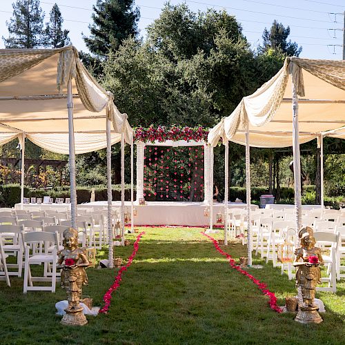 The image shows an outdoor wedding setup with chairs arranged under canopies, an aisle lined with red petals, and a decorated altar at the end.