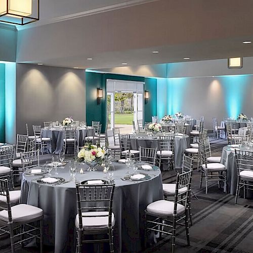 A banquet hall set up with round tables covered in gray tablecloths, decorated with floral centerpieces, and surrounded by chairs.