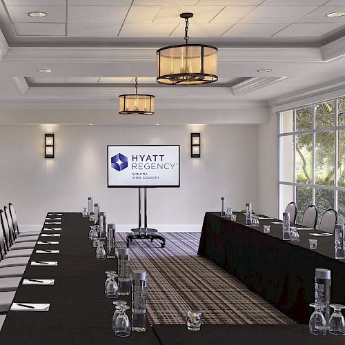 A conference room with U-shaped table setup, water pitchers, pads, pens, and a screen displaying 