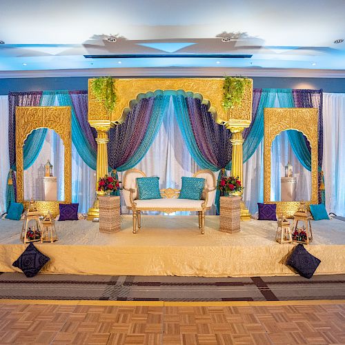 A beautifully decorated stage with a white and gold theme, blue drapes, ornate columns, and a luxurious couch for events or ceremonies.