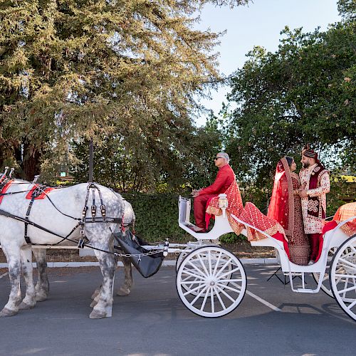 A horse-drawn carriage with two passengers dressed in traditional attire, outside with trees in the background, stopped in an open area.