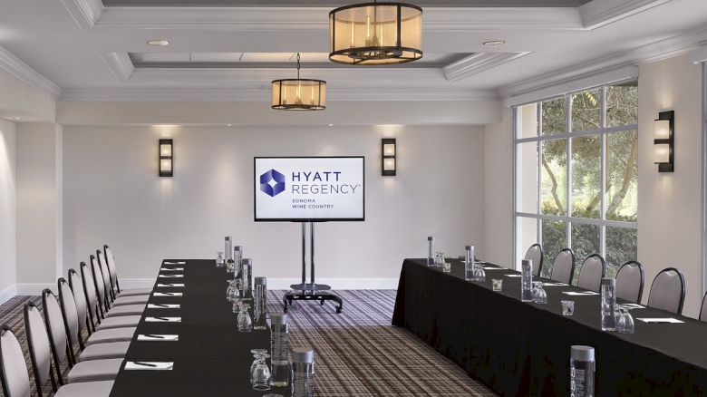 A conference room with a U-shaped table setup, black tablecloths, water pitchers, glasses, chairs, a screen displaying 