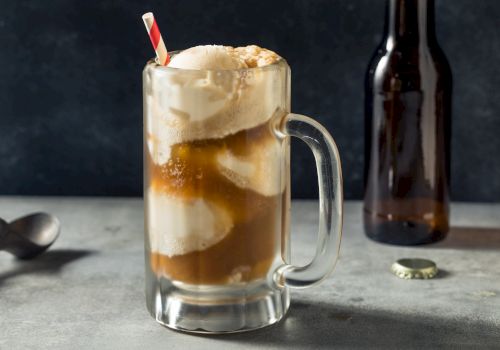 A glass mug filled with a root beer float, topped with vanilla ice cream and a straw, sits next to an empty bottle and bottle cap.