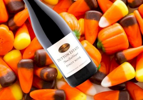 The image shows a bottle of Dutton Estate Pinot Noir wine placed on a background of Halloween-themed candy corn.