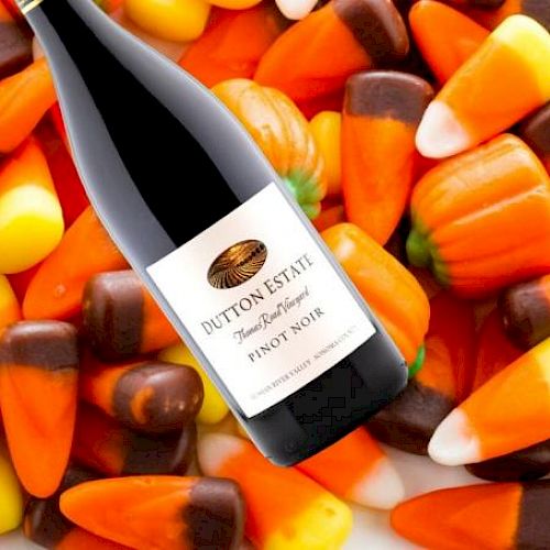 The image shows a bottle of Dutton Estate Pinot Noir wine placed on a background of Halloween-themed candy corn.