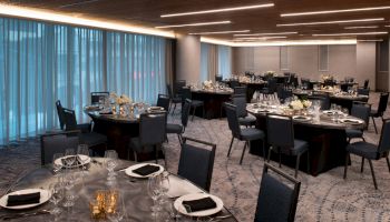 The image shows an elegant banquet hall set up with round tables, each adorned with floral centerpieces, black napkins, and formal dining settings.