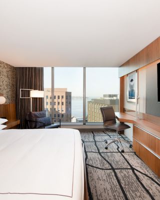 A modern hotel room with a large bed, a desk, a chair, a flat-screen TV, and a window offering a city view, ending the sentence.