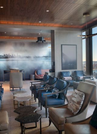 This image shows a modern lounge with comfortable seating, large windows offering a scenic view of water and a Ferris wheel in the background.