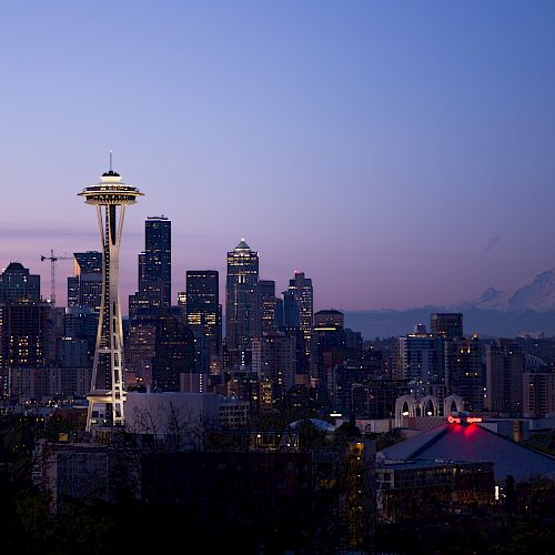 This image shows the Seattle skyline at dusk, featuring the Space Needle prominently with Mount Rainier visible in the background under a fading sky.